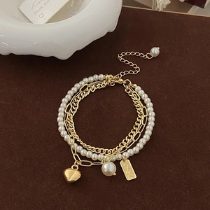 Detailed macro of a triple-layered gold pearl bracelet with heart and tag pendants