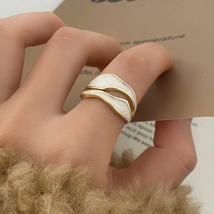Detail of wavy gold ring with cream enamel finish worn on finger for autumn style