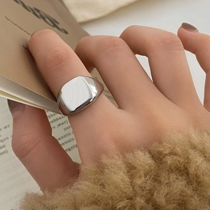 Close-up of minimalist silver square ring worn on index finger with cozy knit sleeve background