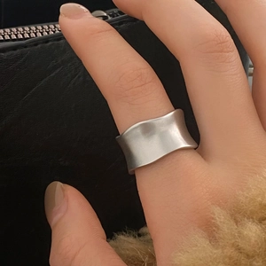 Close-up of matte silver irregular wavy ring worn by a model against a textured background