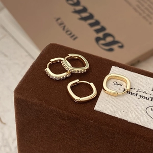 Gros plan de boucles d'oreilles créoles carrées dorées avec pavé de zircons et fini poli