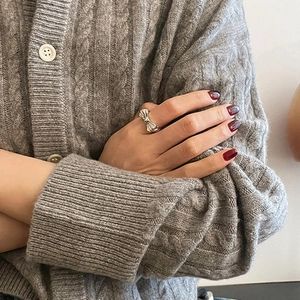 Detail of silver bow knot open ring worn with a grey cable-knit sweater on the finger