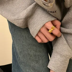 Detailed view of a gold bow ring worn on finger, showcasing its satin finish and design