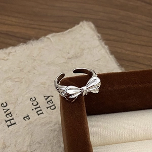 Close-up of polished silver bow ring resting on a velvet jewelry box and wooden desk