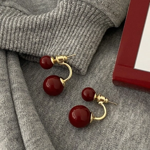 Detail of dual-bead earrings with burgundy pearls and gold metal on knit fabric