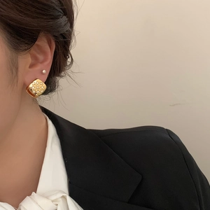 Close-up of golden square stud earrings with zircon inlay worn by a female model