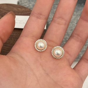 Close-up of pearl stud earrings with crystal halo held between fingertips for scale