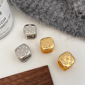 Detail of square gold and silver earrings with star-set cubic zirconia on white surface
