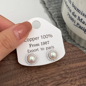 Macro detail of retro sunflower pearl earrings with tiny diamonds on a product display card