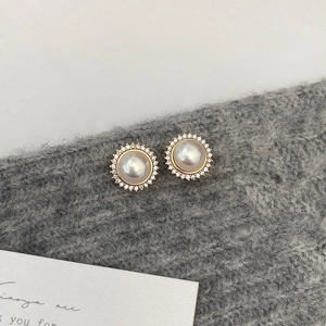 Macro shot of vintage round pearl earrings with zircon halo on grey knit fabric
