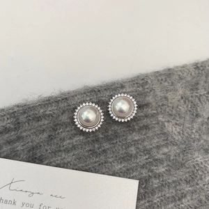 Detailed view of pearl earrings with zircon halo on a gray knit fabric background