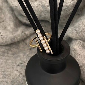 Detail of gold open ring with pearls and pavé zircons displayed on a black diffuser stick