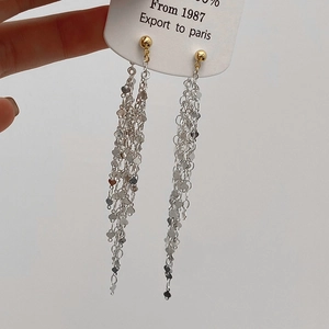 Detail of long tassel earrings with golden studs and layered silver heart sequin chains