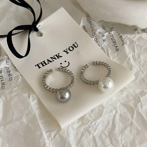 Detail of C-shaped pearl earrings with cubic zirconia inlay on a gift card background