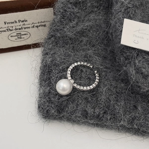 Detailed shot of an open pearl ring with zircons on a textured knitted background