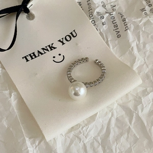 Detailed close-up of a pearl and zircon open ring on a branded white gift label