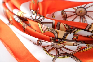 Detailed close-up of orange silk scarf with vintage carriage wheel and chain patterns