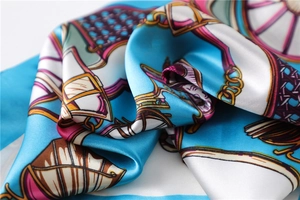 Close-up of silk square scarf featuring elegant blue and gold equestrian carriage patterns