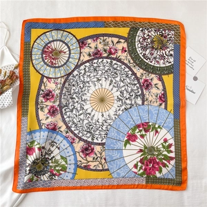 Flat lay of silk scarf featuring floral umbrella patterns and bright orange borders