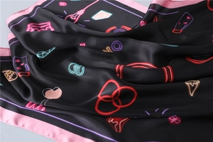 Detailed close-up of silk scarf with neon crown patterns and satin texture finish