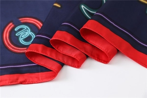 Close-up of a navy silk scarf featuring neon patterns and elegant red piping details
