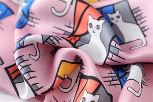 Detailed view of pink silk scarf featuring cartoon cat prints and refined hemmed edges