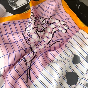 Detail of silk square scarf featuring pink plaid pattern and vibrant orange borders