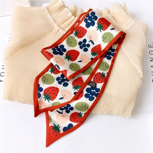 Close-up of strawberry printed twilly silk scarf tied on an apricot pleated blouse