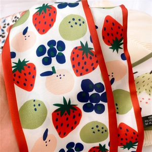 Detail of vibrant fruit pattern scarf with 100% polyester wash label and red stitched edge