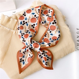 Detail of fall-themed silk scarf with pumpkin print tied on a pleated beige shirt