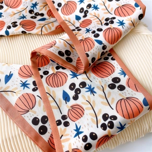 Detailed macro view of silk scarf with orange pumpkins and star leaves on cream satin