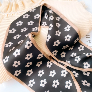 Detailed view of black floral silk scarf with daisy pattern and champagne hem on soft fabric