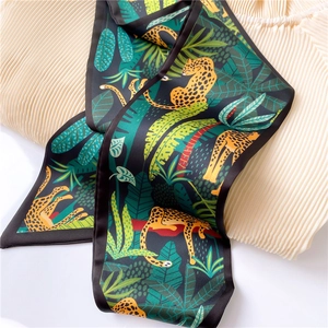 Detailed close-up of a leopard print silk scarf with green tropical leaves on white fabric