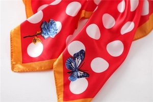 Nahaufnahme des roten Seidenschals mit weißen Punkten, blauen Rosen und gelbem Rand