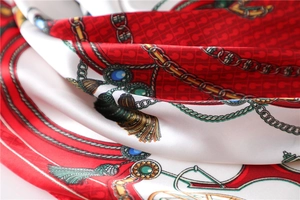 Macro detail of silk scarf featuring gold chains, emerald jewelry, and red luxury patterns