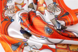 Detailed close-up of vibrant orange silk scarf featuring classic horse chain patterns