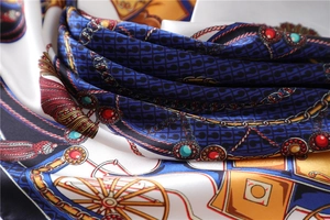 Close-up of luxury silk scarf with gold chains, gemstones, and vintage carriage patterns