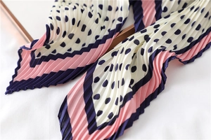 Détail d'un foulard plissé en soie à pois bleu marine avec des bords rayés rose pastel
