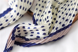 Détail d'un foulard en soie plissé à pois bleu marine sur un tissu en mousseline crème