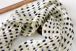Gros plan sur un foulard plissé en soie avec des pois bleu marine sur tissu blanc crème