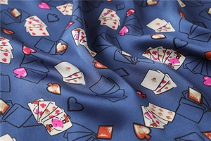 Detail of silk-like scarf featuring heart and spade poker patterns on deep blue fabric