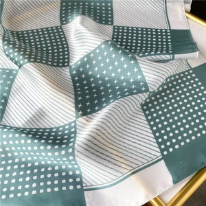 Green and white geometric patchwork silk scarf with dots and star patterns shown on a tray