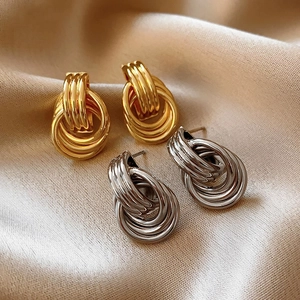 Detail of multi-layered intertwined stud earrings in gold and silver on silk fabric
