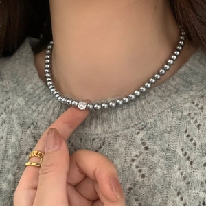 Détail du collier de perles grises avec un pendentif brillant sur un pull en maille