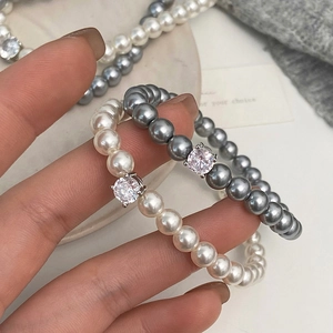 Détail de bracelets en perles blanches et grises avec un grand zircon cubique scintillant