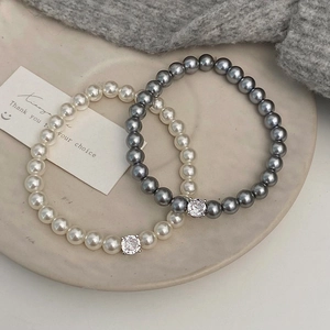 Détail des bracelets en perles crème et grises avec un pendentif en zircon brillant