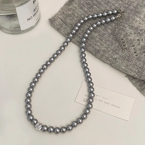 Détail d'un collier de perles grises avec pendentif zircon sur un pull en maille