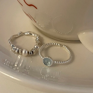 Detail of silver rings with blue cat eye stone and pearls on a ceramic cup edge
