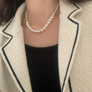 Détail d'un collier de perles blanches dégradées porté avec une veste en tweed chic