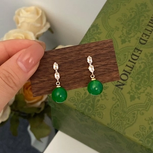 Macro detail of gold green chalcedony drop earrings with sparkling zircon on dark wood
